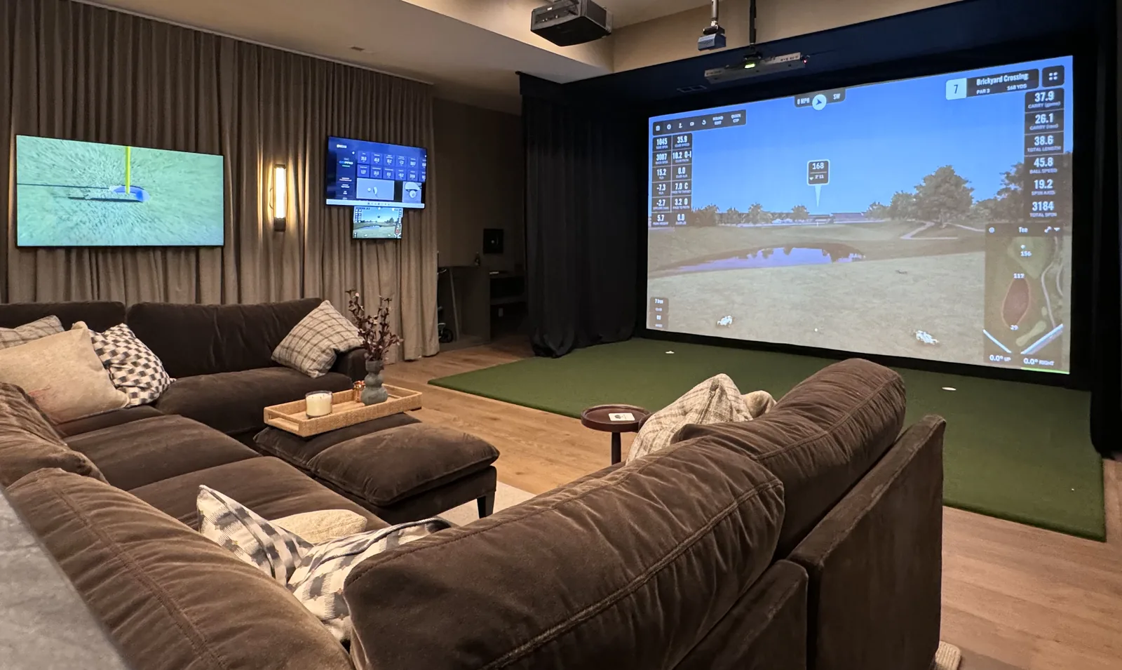 Finished golf simulator lounge with a large screen, hitting turf, and comfortable seating